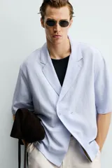 Camisa tipo kimono de corte relaxed fit, color celeste, confeccionada en tejido fluido de viscosa y lino. Presenta cuello con solapas de muesca, manga corta y cierre frontal cruzado con doble botonadura.