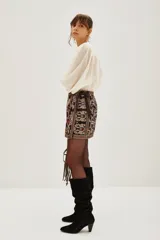 Falda corta tipo portafolio de gabardina liviana, color negro, con bordados florales y de ave en tonos dorados, rosados y morados. Posee un lazo lateral para atar.