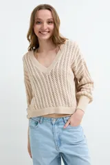 Sweater de tejido calado color beige, con escote en V y mangas largas holgadas con puños ajustados.