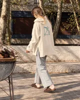 Canguro de felpa color crudo, con capucha, corte amplio, bolsillos delanteros y aberturas laterales en el dobladillo. Presenta un estampado en la espalda con diseño de arco y flecha rodeado de estrellas, y detalles gráficos en las mangas.