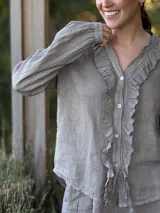 Camisa de lino color gris claro, de manga larga y corte holgado, con cuello mao y detalle de volados en el frente a lo largo de la botonera.