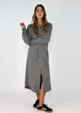 Vestido camisero midi de corte recto y holgado, con cierre frontal de botones, cuello camisero, mangas largas con puños abotonados y bolsillos frontales superiores con solapa.