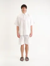 Camisa blanca de manga corta, con cuello clásico, cierre frontal con botones y un bolsillo aplicado en el pecho.