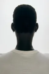 Remera ajustada de punto acanalado suave, color blanco, con cuello redondo ribeteado en picot y tapeta de botones. Es de manga larga.