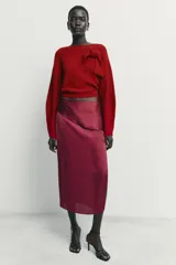 Falda midi de tiro medio confeccionada en tejido satinado con estampado de lunares. Presenta un diseño envolvente con detalle de volante lateral y cierre posterior con cremallera oculta.