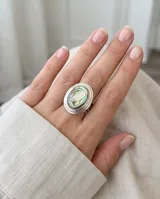 Anillo de plata con diseño ovalado que presenta una incrustación central de piedra abulón con reflejos iridiscentes.