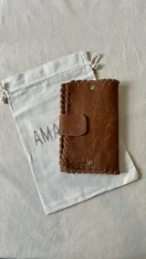 Set de accesorios compuesto por un brazalete rígido abierto, un collar con dije de sol radiante, un par de caravanas onduladas y un par de caravanas tipo fleco, presentados en un sobre de cuero con costuras artesanales.