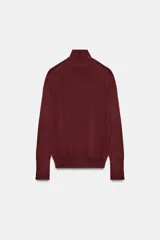 Jersey de punto liso en color beige, con cuello alto y manga larga con detalle de botones metálicos en los puños.