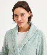 Bata corta en color verde agua, confeccionada en fleece con textura en relieve. Tiene mangas largas, cuello tipo chal y lazo para ajustar en la cintura.