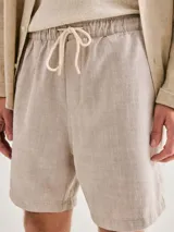 Bermuda de corte recto confeccionada en tela texturizada de color beige, con cintura elástica y cordón ajustable.