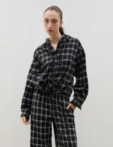 Camisa de manga larga con capucha, confeccionada en tejido liviano con estampado a cuadros. Presenta cierre frontal con botones y lazo regulable en la cintura.