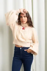 Polera de punto color manteca, con cuello alto, diseño de trenzas y flores en el frente, y mangas globo amplias.