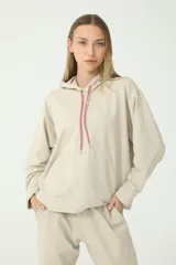 Buzo hoodie color arena, de rústico, con capucha y cordón de ajuste en salmón y verde. Tiene moldería oversize y etiqueta de la marca en la manga derecha con logo Basset 00'S.