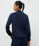 Campera deportiva de cuello alto con cierre frontal, mangas largas con puños elásticos y diseño de corte raglán. Presenta un estilo minimalista y funcional con cintura ajustable.