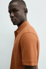 Polo de manga corta color blanco roto, con cuello solapa y cierre frontal de cremallera. Presenta un tejido de piqué estructurado y corte regular fit.