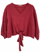 Blusa bordó de lino con escote en V, mangas largas abullonadas con puños elásticos y detalle de nudo en el frente.