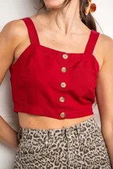 Top corto color rojo, con escote cuadrado y tirantes anchos. Presenta una hilera de botones marrones en el centro del frente.