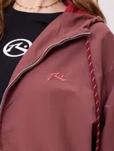 Campera rompevientos color bordó con cierre frontal, capucha con cordones ajustables y franjas laterales en tono más oscuro. Presenta puños elásticos y bolsillos frontales.