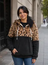 Buzo tipo canguro de tejido polar, con diseño combinado en animal print de leopardo en la parte superior y color negro en la parte inferior. Presenta capucha con cordones ajustables, cierre frontal parcial y bolsillo tipo canguro.