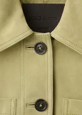Chaqueta corta de piel de ante color verde, con diseño recto, cuello camisero, manga larga, dos bolsillos de parche en la parte delantera y cierre frontal con botones.