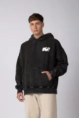Buzo canguro oversize de algodón frisa premium con efecto lavado en color negro. Presenta capucha, bolsillo frontal tipo canguro y estampa blanca en el pecho.