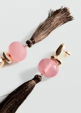 Aros largos compuestos por una pieza metálica dorada, una cuenta esférica de resina rosa y una borla colgante de hilo marrón oscuro.