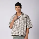 Camisa de manga corta de popelina con patrón a cuadros, calce boxy y largo a la cintura, con bolsillos y canesú cortados en diagonal.