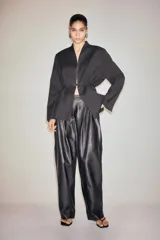 Blazer negro de corte recto con cuello elevado, hombreras y cierre frontal mediante cinturón fino ajustable. Presenta bolsillos delanteros ribeteados y aberturas en los puños.