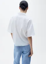 Camisa de manga corta con cuello camisero y cierre frontal de botones. Confeccionada en una mezcla de lino y algodón, presenta un diseño recto y minimalista.