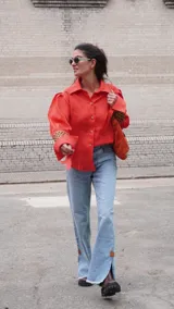 Camisa de lino color naranja vibrante, con cuello camisero, botones frontales y mangas largas abuchonadas con puños anchos que presentan un detalle calado con patrón de puntos.