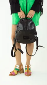 Mochila pequeña de cuero color marrón y beige, con bolsillo externo con cierre, manija superior, bolsillos laterales con broche imán y correas ajustables.