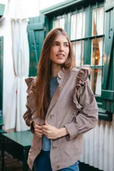 Campera de pana color blanco, de corte oversize, con cuello alto, cierre frontal de botones y volados decorativos en los hombros y cuello.
