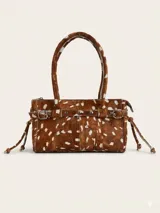 Cartera de mano de estructura rígida, confeccionada en cuero con textura de pelo animal print tipo ciervo. Presenta doble asa superior, cierre principal, y detalle decorativo de tira horizontal con tachas y hebillas metálicas, además de lazos laterales.