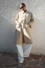 Trench largo de Zara Woman Collection, confeccionado en color beige. Cuenta con cuello de solapa, manga larga, bolsillos frontales de parche y cierre central con botones visibles.