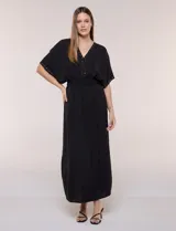 Vestido largo amarillo de corte fluido con escote en V, mangas cortas amplias y apliques de tachas en el escote y puños. Posee cintura elastizada fruncida y falda larga con tajos laterales en el ruedo.