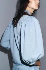 Camisa de denim celeste con cuello solapa, manga corta abullonada y cierre frontal con botones.