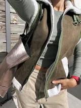 Chaleco negro de cuerina con interior de corderito sintético, bolsillos frontales y hebillas decorativas.