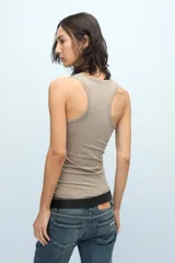 Musculosa fitted color tostado, confeccionada en pima de algodón peruano con lycra. Presenta escote en U, espalda deportiva y cartera de botones a tono personalizados. Incluye bordado marcario a tono en el frente.