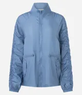 Campera deportiva tipo parka de microfibra en color azul, con cuello alto, cierre frontal por cremallera y mangas largas con puños elásticos. Presenta un diseño con fruncido lateral ajustable y corte amplio.