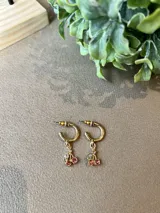 Aros dorados tipo argolla con dije de cerezas rojas y hojas blancas.