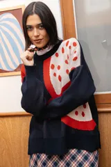 Buzo tejido de punto con diseño gráfico de granada en colores rojo y crema sobre base azul marino. Presenta silueta oversize, cuello redondo y calce relajado.