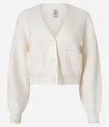 Cardigan corto de punto color beige claro, con escote en V, manga larga abullonada y cierre frontal de botones. Posee bolsillos delanteros tipo parche.