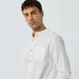 Camisa blanca de lino con cuello mao, manga larga con puños abotonados y bolsillo de parche en el pecho. Cierre frontal con botones a tono.