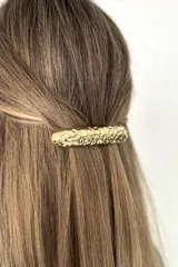 Broche para el cabello de metal dorado con diseño de superficie texturizada e irregular.