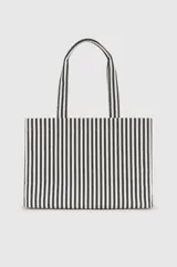 Bolso tipo shopper de diseño rectangular y amplio, confeccionado en tela con patrón de rayas verticales en color blanco y negro. Cuenta con dos asas superiores para llevar al hombro y detalle de aplique metálico con monograma en el centro.