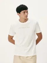 Camiseta blanca de algodón con cuello redondo y mangas cortas. Estampa rectangular con borde negro que contiene la frase "NATURAL ATMOSPHERE" en letras mayúsculas y una imagen de montañas y mar.