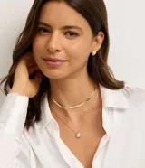 Conjunto de bisutería compuesto por un collar tipo cadena plana, un collar de cadena fina con dije de perla y un par de aros pequeños con perla aplicada. Presenta un acabado en tono dorado.