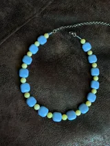 Collar corto de cuentas, compuesto por cuentas cuadradas celestes intercaladas con cuentas esféricas amarillas pequeñas.