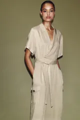 Mono largo de cuello solapa y escote en pico cruzado, con mangas cortas. Presenta bolsillos laterales de plastrón con solapa y botones, y un cinturón del mismo tejido para ajustar en la cintura. Cierre frontal con cremallera y botón interior.