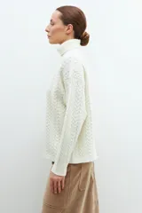 Polera color crudo con cuello alto y tejido con diseño de trenzas.